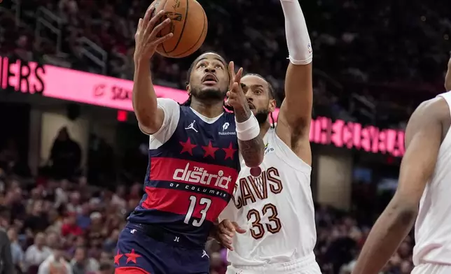 Washington Wizards guard Sharife Cooper (13) goes to the basket past Cleveland Cavaliers forward Olivier Sarr (33) in the second half of an NBA basketball game in Cleveland, Sunday, April 12, 2026. (AP Photo/Sue Ogrocki)