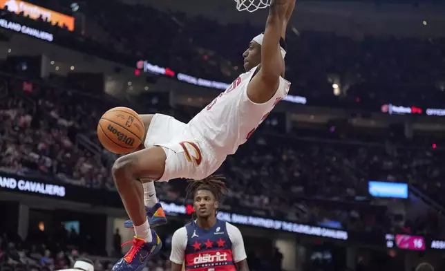 Cleveland Cavaliers forward Nae'qwan Tomlin hangs from the basket after dunking in front of Washington Wizards guard Jamir Watkins (5) in the second half of an NBA basketball game in Cleveland, Sunday, April 12, 2026. (AP Photo/Sue Ogrocki)
