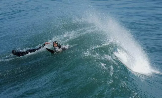 Surfers pass under a wave alongside the Imperial Beach pier Wednesday, March 11, 2026, in Imperial Beach, Calif. (AP Photo/Gregory Bull)
