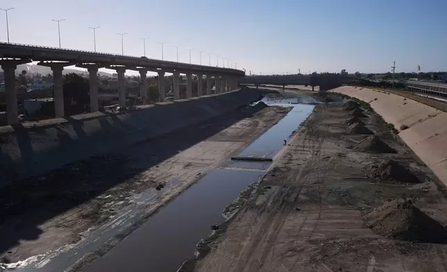 A man walks along the an aqueduct holding the Tijuana River as it arrives to the border and enters the United States, above, from Tijuana, Mexico, Wednesday, April 8, 2026. (AP Photo/Gregory Bull)