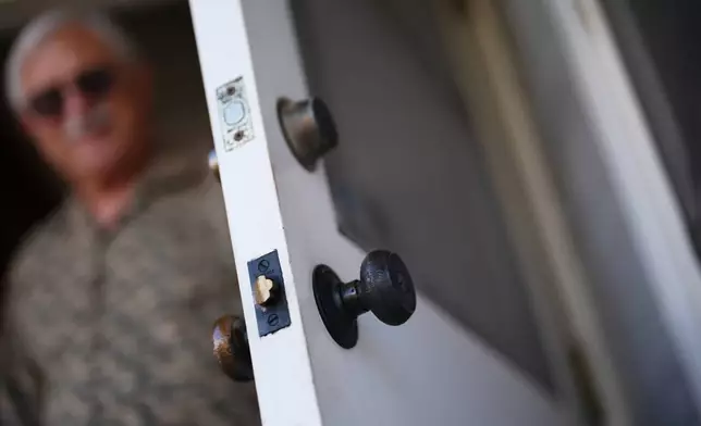 Steve Egger looks out from his door where the outer doorknob has turned black at his home Friday, March 6, 2026, in San Diego. (AP Photo/Gregory Bull)