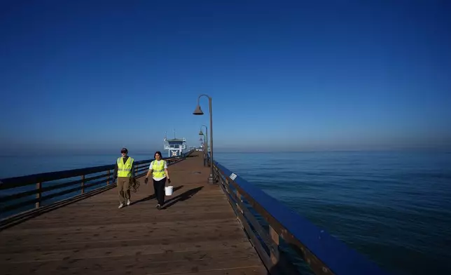 Justin Hamlin, left, and Maddie Tibayan, walk along the Imperial Beach pier after gathering a sample of seawater as part of a research team from the University of California, San Diego, Wednesday, March 11, 2026, in Imperial Beach, Calif. (AP Photo/Gregory Bull)