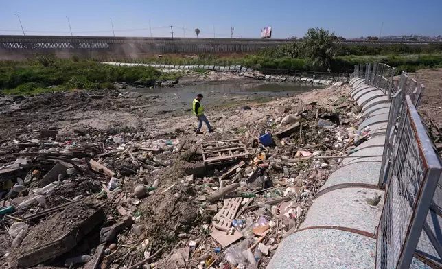 Oscar Romo walks among debris that has been captured by a trash boom installed in the Tijuana River at the border near where the river enters the United States from Tijuana, Mexico, Wednesday, April 8, 2026, in San Diego, Calif. (AP Photo/Gregory Bull)