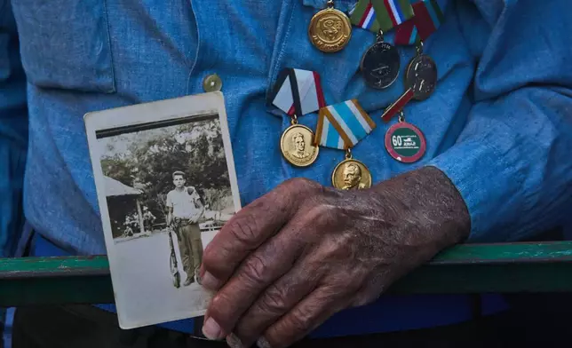 Militiaman Rene Hernandez Delgado holds a photo of his younger self during a celebrations marking the 65th anniversary of the proclamation declaring the Cuban Revolution socialist, in Havana, Cuba, Thursday, April 16, 2026. (AP Photo/Ramon Espinosa)