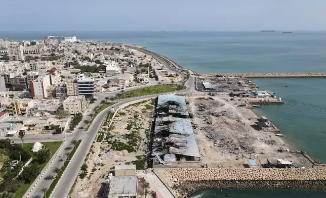 Backdropped by ships in the Strait of Hormuz, damage, according to local witnesses caused by several recent airstrikes during the U.S.-Israel military campaign, is seen on a fishing pier in the port of Qeshm island, Iran, Monday, April 13, 2026. (AP Photo/Asghar Besharati)