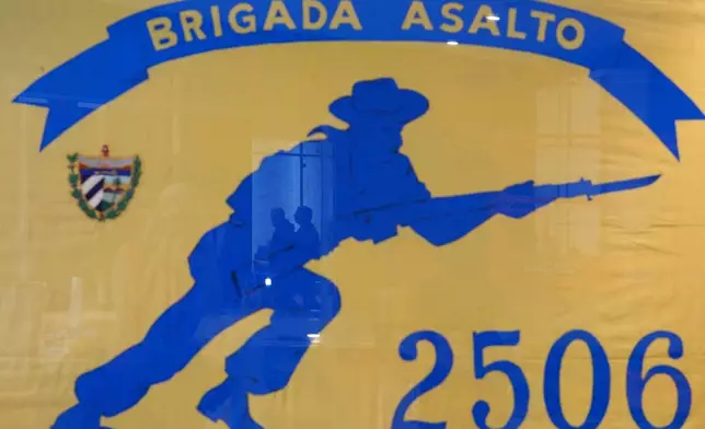 People are reflected in a framed Brigade 2506 flag, as preparation work continues for the reopening of the Bay of Pigs Museum in a new and expanded space in Miami's Little Havana neighborhood, Tuesday, April 7, 2026. (AP Photo/Rebecca Blackwell)