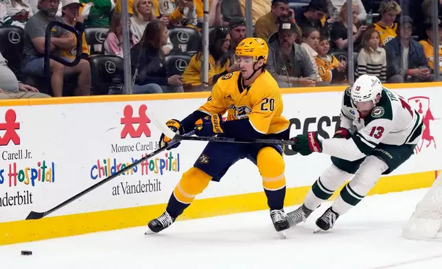 Nashville Predators defenseman Justin Barron (20) and Minnesota Wild center Yakov Trenin (13) chase the puck during the second period of an NHL hockey game Saturday, April 11, 2026, in Nashville, Tenn. (AP Photo/Mark Humphrey)