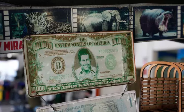 A plaque made from a dollar bill bearing the face of the late drug trafficker Pablo Escobar is displayed alongside photographs of wildlife at a souvenir store in Puerto Triunfo, Colombia, Thursday, April 23, 2026. (AP Photo/Fernando Vergara)