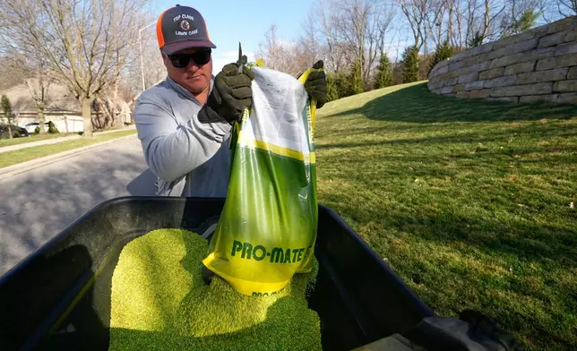 Top Class Lawn Care owner Jake Wilson dumps fertilizer into a hopper before applying it to a lawn Thursday, March 26, 2026, in Kansas City, Mo. (AP Photo/Charlie Riedel)