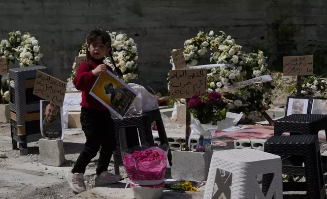 A young girl carries a portrait of a killed Hezbollah fighter at a mass grave where civilians and Hezbollah fighters killed in Israeli airstrikes are temporarily buried in the southern port city of Sidon, Lebanon, Tuesday, April 14, 2026. (AP Photo/Mohammed Zaatari)