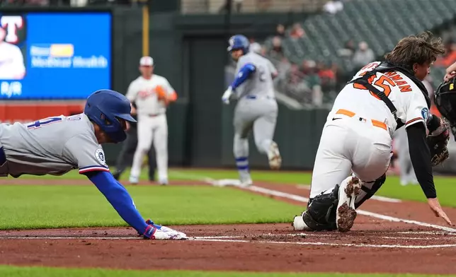Texas Rangers' Brandon Nimmo, left, scores past Baltimore Orioles catcher Adley Rutschman (35) as Rangers' Jake Burger, back right, runs toward first base during the first inning of a baseball game, Monday, March 30, 2026, in Baltimore. (AP Photo/Stephanie Scarbrough)
