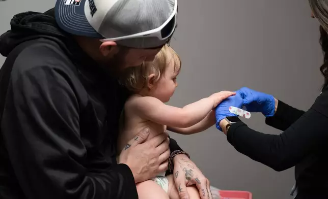 Daren Chandler holds his 12-month-old daughter as she has blood drawn for testing, before receiving a measles shot at Tiger Pediatrics in Easley, S.C., on March 17, 2026. (AP Photo/Mary Conlon)