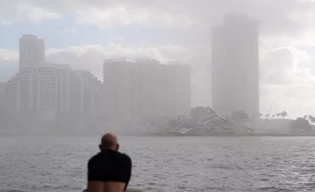 A man, with his shirt pulled up to cover his nose against dust, looks toward the debris following the controlled implosion of the former Mandarin Oriental Hotel on Brickell Key, Sunday, April 12, 2026, in Miami. (AP Photo/Rebecca Blackwell)