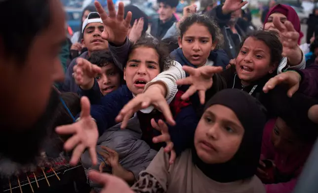 Displaced families extend their hands while waiting for donated food beside the tents they use as shelters after fleeing Israeli bombardment in southern Lebanon, in Beirut, Lebanon, Thursday, April 9, 2026. (AP Photo/Emilio Morenatti)