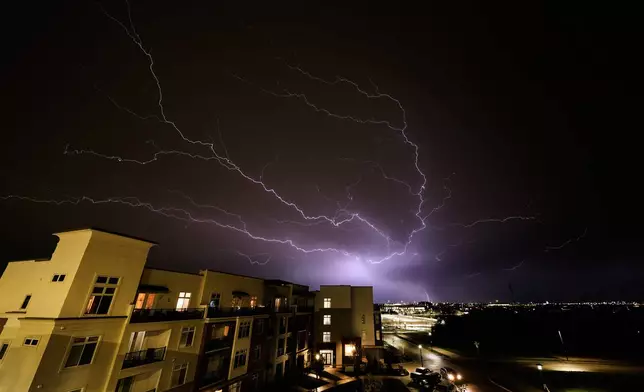 Lightning flashes beyond an apartment building as a thunderstorm passes in the distance Monday, April 13, 2026, in Lenexa, Kan. (AP Photo/Charlie Riedel)