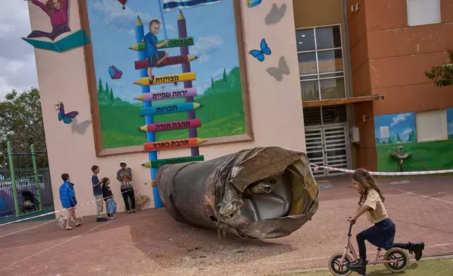 FILE - Children play beside a fragment of an Iranian ballistic missile that landed in a schoolyard in the Israeli settlement of Peduel in the West Bank, March 23, 2026. (AP Photo/Ohad Zwigenberg, File)