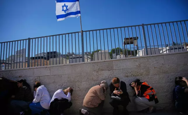 FILE- Mourners take cover while air-raid sirens warn of incoming missiles launched by Iran toward Israel during the funeral of Sarah Elimelech and her daughter Ronit, who were killed in an Iranian missile attack, in Beit Shemesh, Israel, March 2, 2026. (AP Photo/Ohad Zwigenberg, File)