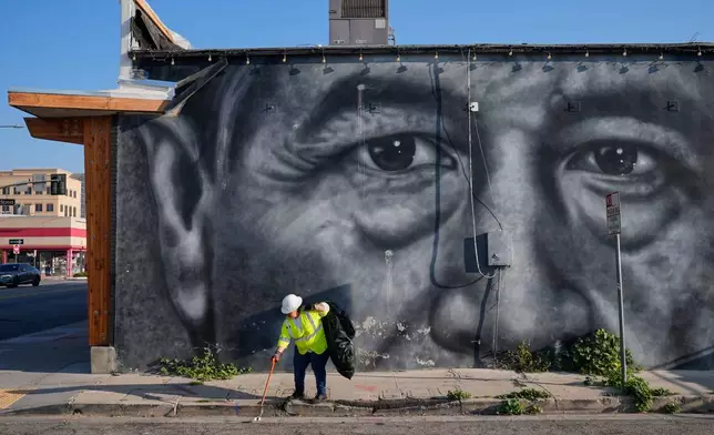 FILE - A sanitation worker picks up trash next to a mural of César Chavez in Bakersfield, Calif., March 19, 2026. (AP Photo/Godofredo A. Vásquez, File)