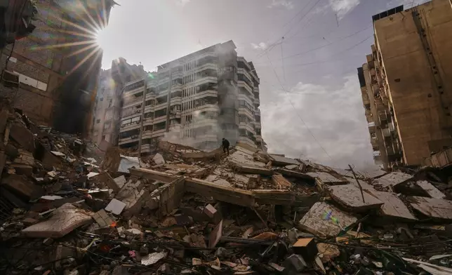 FILE - A man stands atop the rubble as smoke rises from a building destroyed in an Israeli airstrike in Dahiyeh, Beirut's southern suburbs, Lebanon, March 14, 2026. (AP Photo/Hassan Ammar)