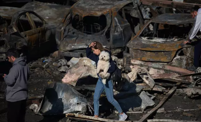 A woman holds her dog as she walks past burned cars a day after an Israeli airstrike in Beirut, Lebanon, Thursday, April 9, 2026. (AP Photo/Emilio Morenatti)