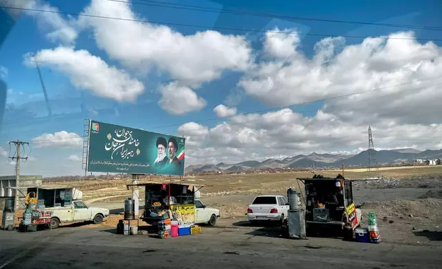 Vendors sell fruit, food and hot beverages along Road 2 next to a billboard depicting Iran's Supreme Leader Mojtaba Khamenei, right, and his father, slain Ayatollah Ali Khamenei, near Zanjan, Iran, Thursday, April 9, 2026. (AP Photo/Francisco Seco)