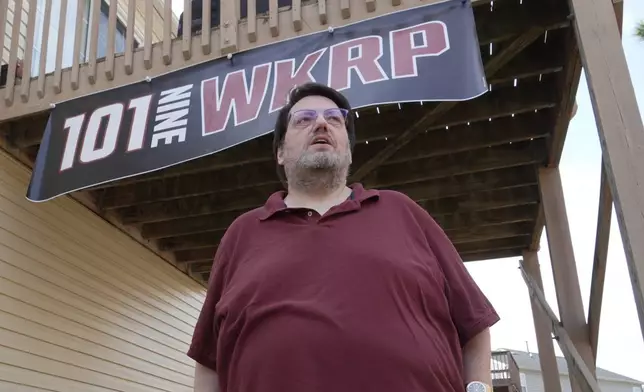 D.P. McIntire stands beneath a WKRP banner in the backyard of his home in Raleigh, N.C., on Thursday, April 2, 2026. (AP Photo/Allen G. Breed)