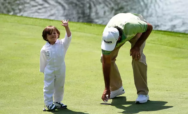 Max Homa, right, picks up a putt by his son, Cam Andrew, on the eighth hole during par-3 contest ahead of the Masters golf tournament at the Augusta National Golf Club, Wednesday, April 8, 2026, in Augusta, Ga. (AP Photo/Gerald Herbert)