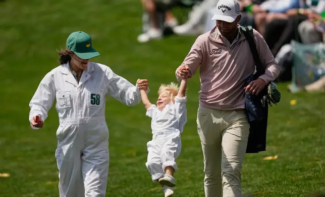 Sam Burns, right, and wife, Caroline Campbell Burns, left, carry their son, Bear, on the eighth hole during par-3 contest ahead of the Masters golf tournament at the Augusta National Golf Club, Wednesday, April 8, 2026, in Augusta, Ga. (AP Photo/Gerald Herbert)