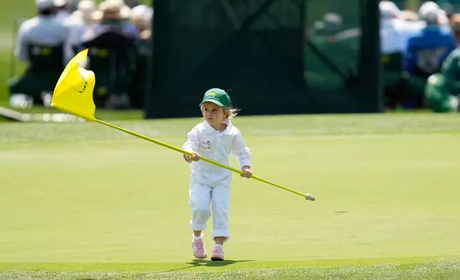 Bernhard Langer's grand daughter, Stella Rose carries the flag pin on the first hole during par-3 contest ahead of the Masters golf tournament at the Augusta National Golf Club, Wednesday, April 8, 2026, in Augusta, Ga. (AP Photo/Ashley Landis)
