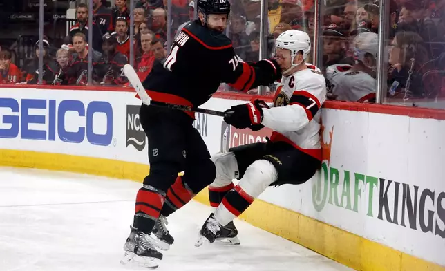 Carolina Hurricanes' Jaccob Slavin, left, checks Ottawa Senators' Brady Tkachuk (7) into the boards during the second overtime of Game 2 of an NHL hockey Stanley Cup first-round playoff series in Raleigh, N.C., Monday, April 20, 2026. (AP Photo/Karl DeBlaker)
