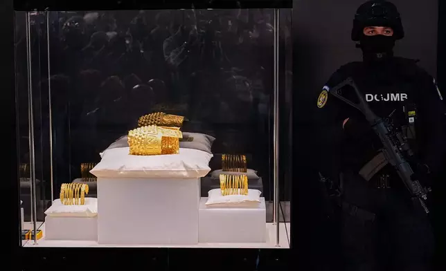 An armed gendarme stands by Dacian gold items, a 2,500-year-old helmet and wristbands, stolen from a museum in the Netherlands and then recovered by Dutch authorities, during a press conference after being returned, at the National Museum of Romanian History, in Bucharest, Romania, Tuesday, April 21, 2026. (AP Photo/Andreea Alexandru)