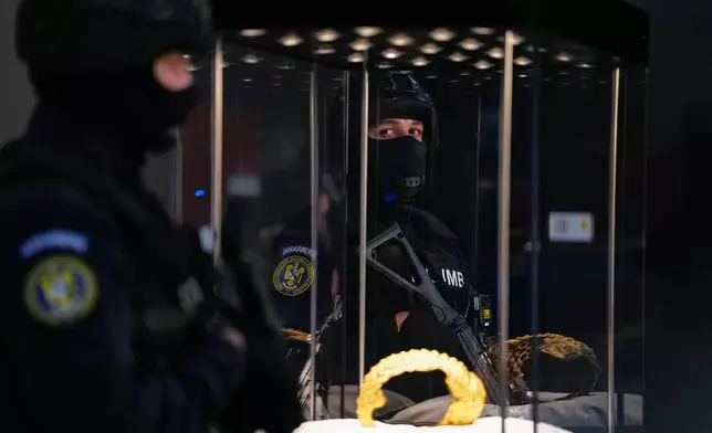 Armed gendarmes stand by Dacian gold items, a 2,500-year-old helmet and wristbands, stolen from a museum in the Netherlands and then recovered by Dutch authorities, during a press conference after being returned, at the National Museum of Romanian History, in Bucharest, Romania, Tuesday, April 21, 2026. (AP Photo/Andreea Alexandru)