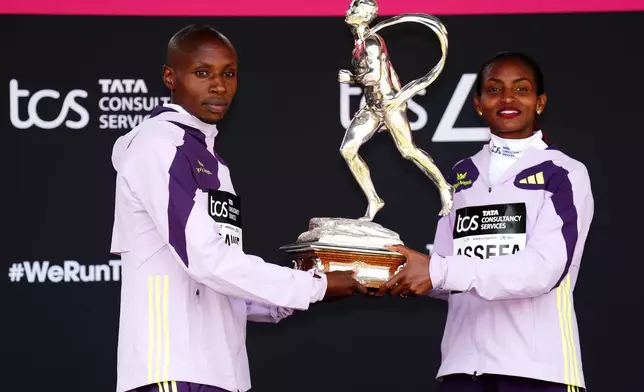 Sebastian Sawe from Kenya, winner of the men's race, and Tigst Assefa of Ethiopia winner of the women's race, celebrate with the sporting life trophy on the podium after the London Marathon, Sunday April 26, 2026. (John Walton/PA via AP)