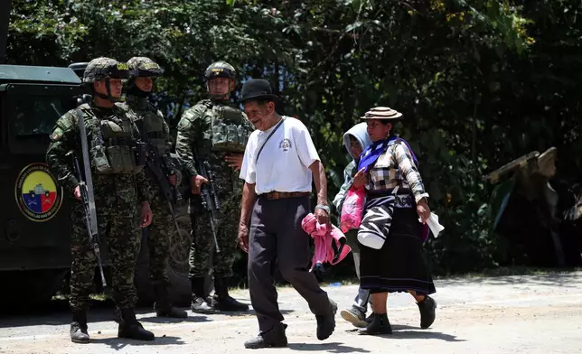 People walk past soldiers guarding at the site of the attack on the Pan-American Highway in Cajibio, Colombia, Sunday, April 26, 2026, a day after an assault that killed at least 20 people and that authorities blamed on dissident groups of the former FARC rebels. (AP Photo/Santiago Saldarriaga)