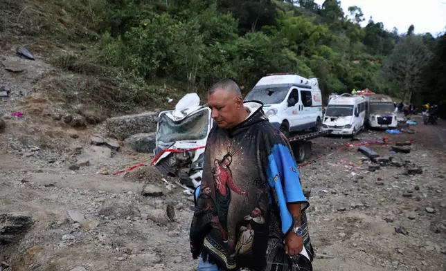 A man walks past vehicles damaged in an attack on the Pan-American Highway in Cajibio, Colombia, Sunday, April 26, 2026, where at least a dozen people were killed in an attack authorities blamed on dissident groups of the former FARC rebels. (AP Photo/Santiago Saldarriaga)
