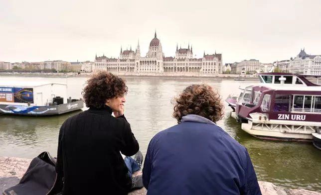 Hungarian students Kristof, left, 19 years-old, and Vincent, 20 years-old, paint by the Danube river, backdropped by the parliament building in Budapest, Hungary, Monday, April 13, 2026, after Peter Magyar's Tisza party defeated Prime Minister Viktor Orban's Fidesz party in the country's parliamentary elections. (AP Photo/Petr David Josek)