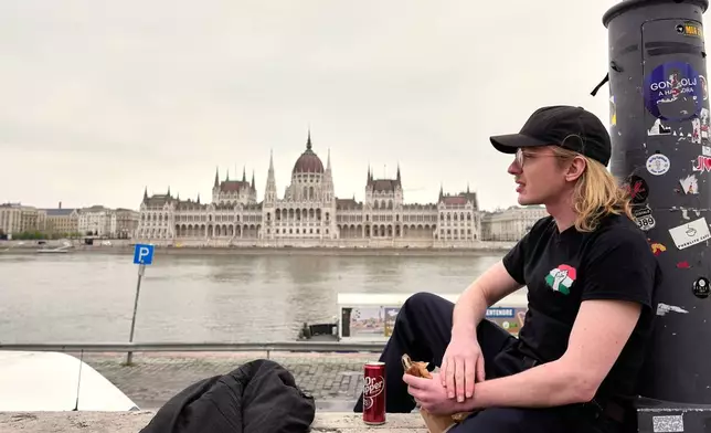 Milan, 26 years-old, relaxes by the Danube river, backdropped by the parliament building in Budapest, Hungary, Monday, April 13, 2026, after Peter Magyar's Tisza party defeated Prime Minister Viktor Orban's Fidesz party in the country's parliamentary elections. (AP Photo/Petr David Josek)