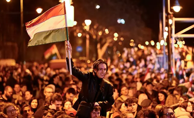 A man waves a Hungarian flag as he celebrates in the streets after the announcement of partial results of the Hungarian parliamentary in Budapest, Hungary, Sunday, April 12, 2026. (AP Photo/Denes Erdos)