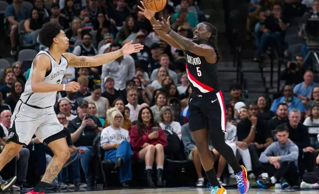 Portland Trail Blazers guard Jrue Holiday (5) grabs the ball ahead of San Antonio Spurs guard Dylan Harper during the first half of an NBA basketball game, Wednesday, April 8, 2026, in San Antonio. (AP Photo/Darren Abate)