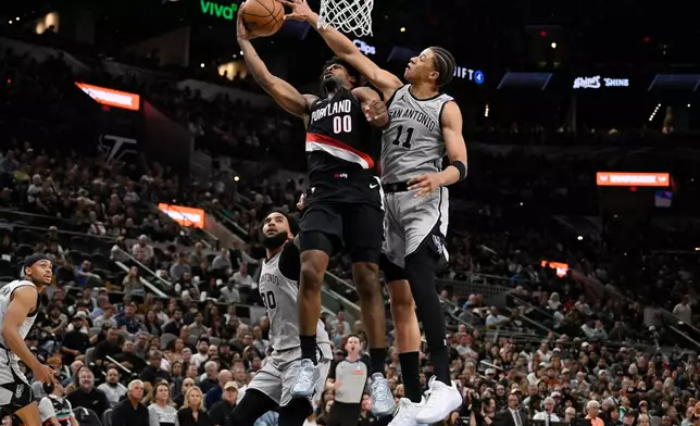Portland Trail Blazers guard Scoot Henderson (00) is fouled by San Antonio Spurs forward Carter Bryant during the first half of an NBA basketball game, Wednesday, April 8, 2026, in San Antonio. (AP Photo/Darren Abate)