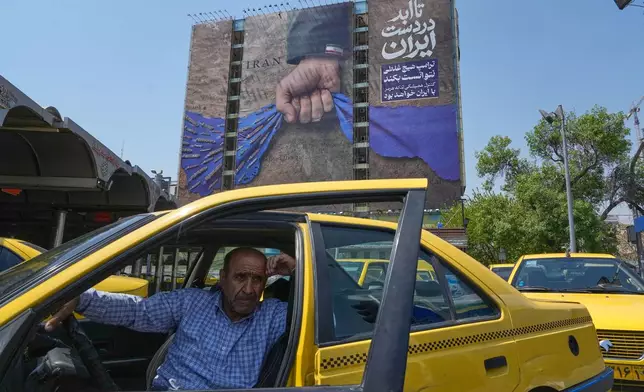 A taxi driver waits for passengers in front of a billboard that shows a graphic depicting a military personnel's hand holding the Strait of Hormuz in his fist with signs which read in Farsi: "In Iran's hands forever," "Trump couldn't do a damn thing," "The control of Strait of Hormuz will be Iran's forever," in Vanak Square in northern Tehran, Iran, Thursday, April 16, 2026. (AP Photo/Vahid Salemi)