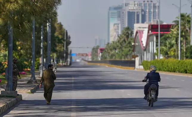 An army soldier, left, walks as police officer drives motorcycle on an empty road ahead of second round of negotiations between the U.S. and Iran, in Islamabad, Pakistan, Monday, April 20, 2026. (AP Photo/Anjum Naveed)