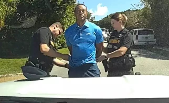 In this image from police body camera video released by the Martin County, Fla., Sheriff's Office, golfer Tiger Woods is taken into custody by sheriff's deputies following a car crash in Jupiter Island, Fla., Friday, March 27, 2026. (Martin County Sheriff's Office via AP)