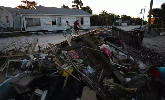 FILE - People bike past damaged homes and debris left by Hurricane Milton, on the sand-coated main road of southern Manasota Key, already cleared of feet of sand, in Englewood, Fla., Oct. 13, 2024. (AP Photo/Rebecca Blackwell, File)