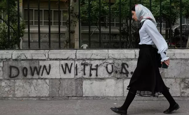A woman walks past an anti-U.S. graffiti painted on the wall of the Tehran University on Enqelab-e-Eslami (Islamic Revolution) street in downtown Tehran, Iran, Saturday, April 25, 2026. (AP Photo/Vahid Salemi)