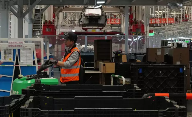 A worker transfers compartments at the Tesla Model Y production lines at the Tesla Gigafactory assembly plant during a media organized tour, in Shanghai, China, Tuesday, April 14, 2026. (AP Photo/Andy Wong)