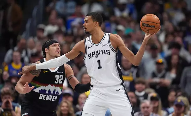 San Antonio Spurs center Victor Wembanyama, right, looks to pass the ball as Denver Nuggets forward Aaron Gordon defends during overtime of an NBA basketball game Saturday, April 4, 2026, in Denver. (AP Photo/David Zalubowski)