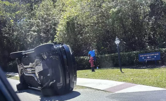 Golfer Tiger Woods stands by his overturned vehicle in Jupiter Island, Fla., Friday, March 27, 2026. (AP Photo/Jason Oteri)