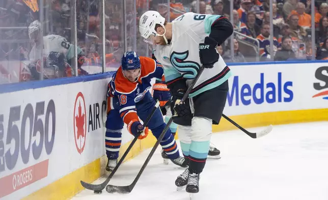 Seattle Kraken's Adam Larsson (6) and Edmonton Oilers' Zach Hyman (18) battle for the puck during the second period of an NHL game, in Edmonton, Tuesday March 31, 2026. (Jason Franson/The Canadian Press via AP)