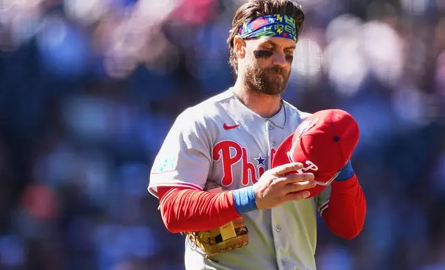 Philadelphia Phillies first baseman Bryce Harper puts on his hat and heads to his position after lining out to end the top of the eighth inning of a baseball game against the Colorado Rockies Sunday, April 5, 2026, in Denver. (AP Photo/David Zalubowski)